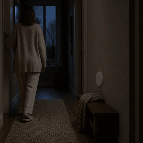 Frau betritt den dunklen Flur und das LumiBeam Nachtlicht schaltet sich per Bewegungsmelder ein