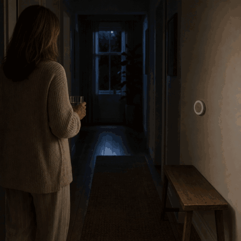 Frau betritt den dunklen Flur und das LumiBeam Nachtlicht schaltet sich per Bewegungsmelder ein